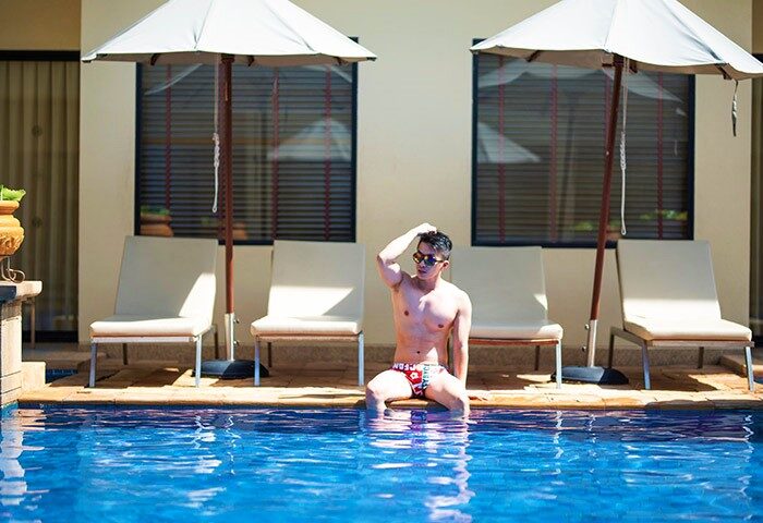 Holiday Inn Resort Phuket gay-friendly pool scene. Man in swimwear sits by the pool, lounge chairs and umbrellas in the background.