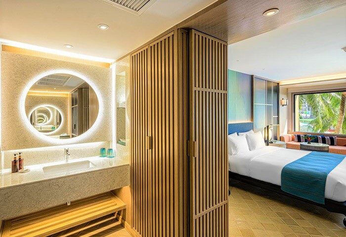 Holiday Inn Resort Phuket gay-friendly hotel room. Modern bathroom with round mirror, and a bedroom with a bed and window view.