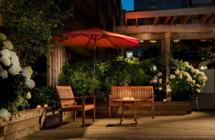 Holiday Inn Toronto Downtown Centre's gay-friendly outdoor patio at night. Wooden benches, table, umbrella, and lush greenery. Relaxing space.