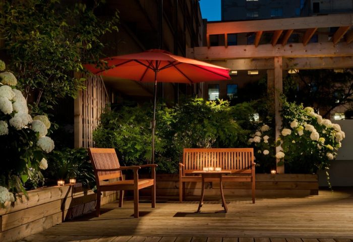 Holiday Inn Toronto Downtown Centre's gay-friendly outdoor patio at night. Wooden benches, table, umbrella, and lush greenery. Relaxing space.