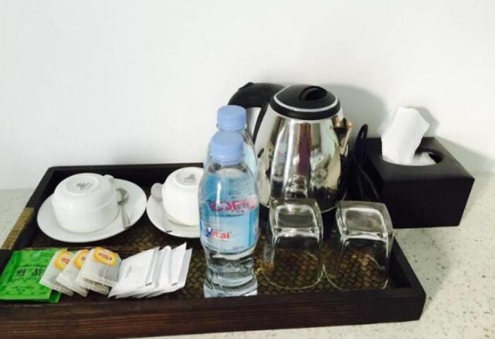 Home Chic Hotel's gay-friendly amenities: tea, water, kettle, glasses, and tissues on a tray. A welcoming touch for gay travelers.