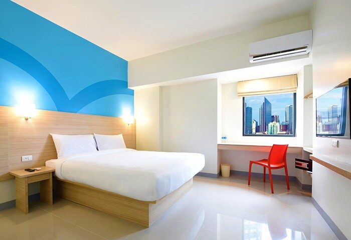 Hop Inn Hotel Makati Avenue Manila room. Gay-friendly hotel with bed, desk, chair, TV, and city view. Modern, clean, and comfortable for travelers.