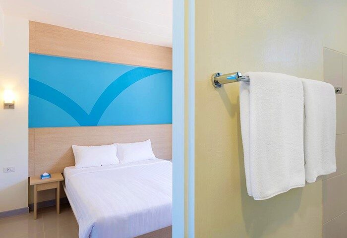 Hop Inn Hotel Makati Avenue Manila room. Gay-friendly hotel with bed, blue accent wall, bedside table, & bathroom towels. Manila travel.