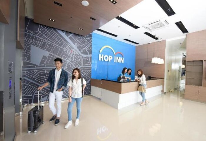 Lobby of Hop Inn Hotel Makati Avenue Manila, a gay-friendly hotel. Guests checking in at the front desk. Modern design with map mural.