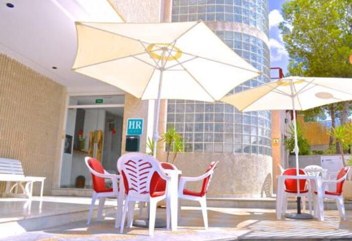 Hostal Residencia Molins Park outdoor seating. Gay-friendly hotel with tables, chairs, and umbrellas. Ideal for gay men travel advice.