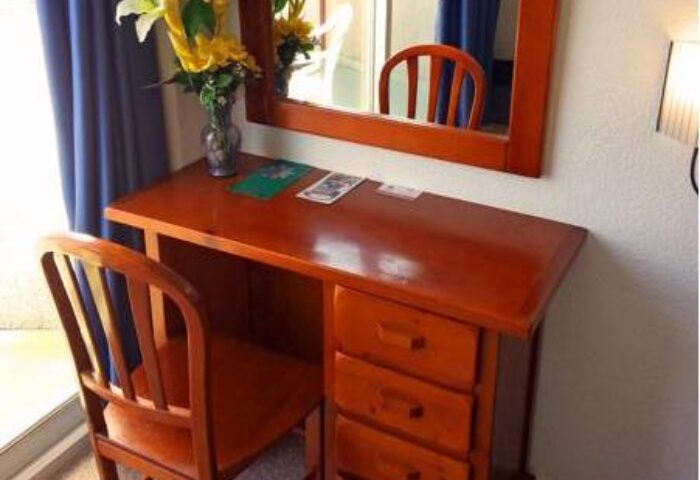 Desk at Hostal Residencia Molins Park, a gay-friendly hotel. Wood desk, chair, mirror, flowers, and blue curtains in the room.