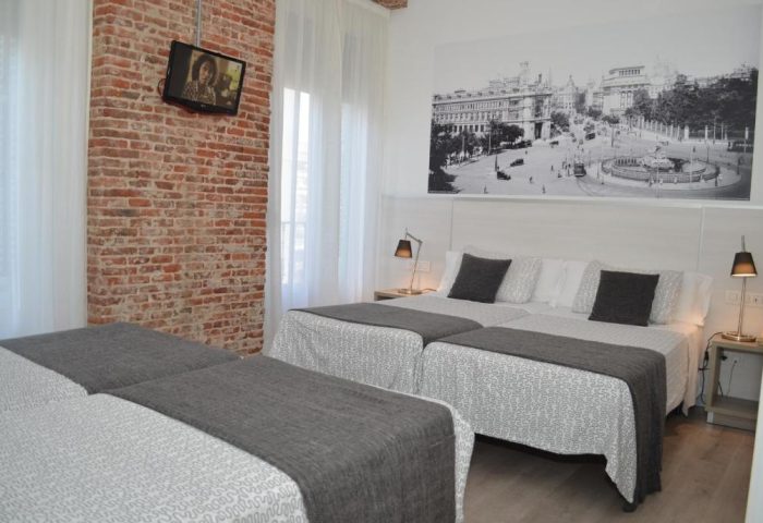 Gay-Friendly Hostal San Lorenzo room with twin beds, brick wall, and TV. Black and white Madrid landmark photo above beds. Gay travel lodging.