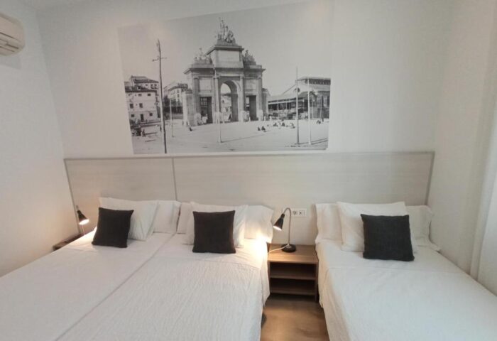 Gay-Friendly Hotel Hostal San Lorenzo room with twin beds, nightstand, lamps, and a black and white photo of a city gate above the headboard.