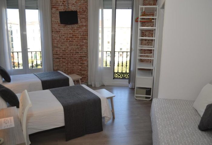 Gay-Friendly Hotel Hostal San Lorenzo room with twin beds, exposed brick wall, balcony, and modern decor. A comfortable stay for gay travelers.