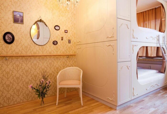 Hostel die Wohngemeinschaft room featuring a chair, ornate wallpaper, and a unique bunk bed design. Gay-friendly hotel interior.