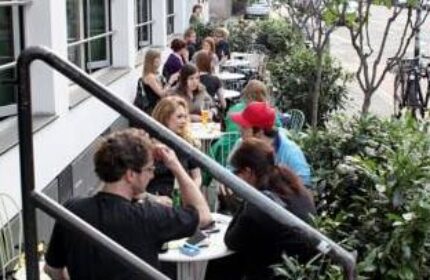 People at tables outside Die Wohngemeinschaft, a gay-friendly hostel. A popular spot for travelers in a relaxed setting.