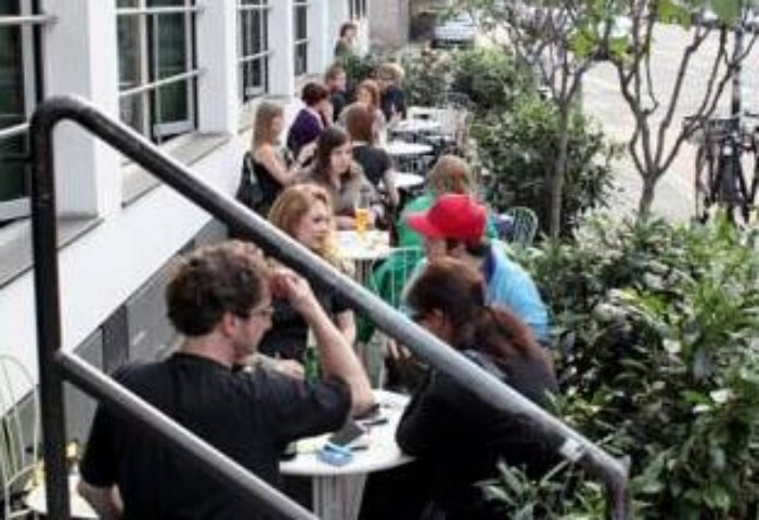 People at tables outside Die Wohngemeinschaft, a gay-friendly hostel. A popular spot for travelers in a relaxed setting.