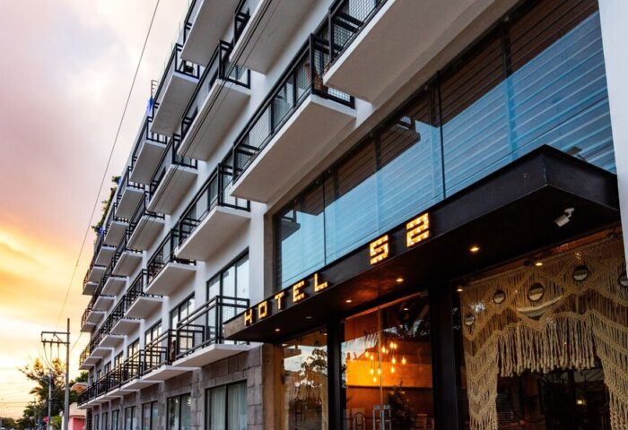 Hotel 52, a gay-friendly hotel. Exterior view of the hotel with balconies. The name Hotel 52 is lit above the entrance. Modern architecture.