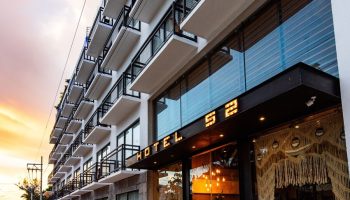 Hotel 52, a gay-friendly hotel. Exterior view of the hotel with balconies. The name Hotel 52 is lit above the entrance. Modern architecture.