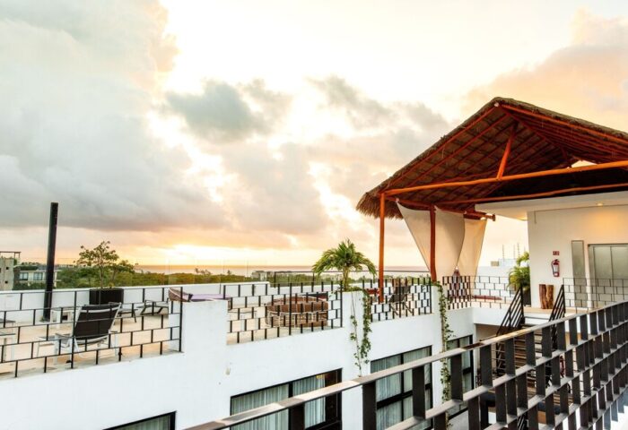 Hotel 52, a gay-friendly hotel. Rooftop view with a thatched roof cabana, seating area, and ocean view at sunset. Ideal for gay travel.