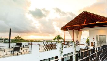Hotel 52, a gay-friendly hotel. Rooftop view with a thatched roof cabana, seating area, and ocean view at sunset. Ideal for gay travel.