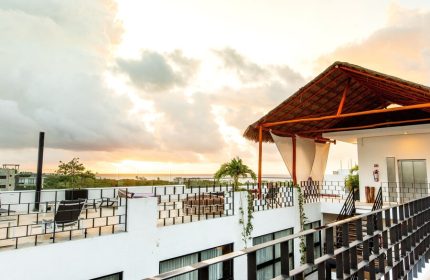 Hotel 52, a gay-friendly hotel. Rooftop view with a thatched roof cabana, seating area, and ocean view at sunset. Ideal for gay travel.