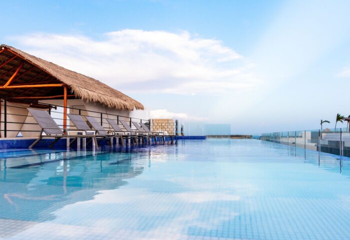 Hotel 52, a gay-friendly hotel. Infinity pool view with lounge chairs under a thatched roof. Perfect for gay travel and relaxation.