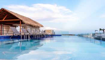 Hotel 52, a gay-friendly hotel. Infinity pool view with lounge chairs under a thatched roof. Perfect for gay travel and relaxation.