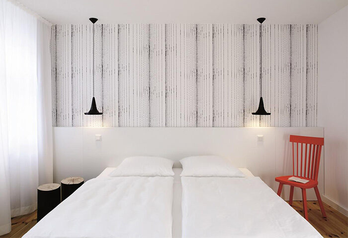 Hotel AMANO room: double bed, stylish wallpaper, and modern black lamps. Pet-friendly, gay-friendly hotel with unique design elements.