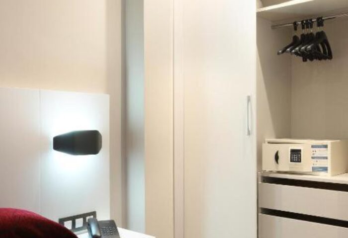 Hotel Alameda's gay-friendly room with a red bedspread, bedside table, phone, and closet with safe. A comfortable stay for gay travelers.