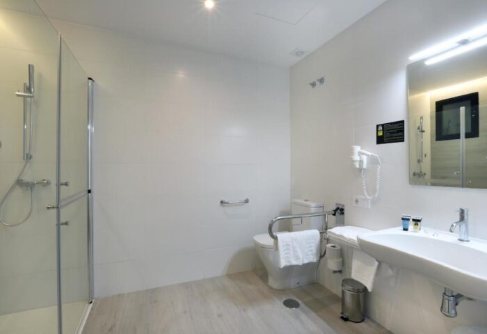 Hotel Alameda gay-friendly bathroom. Accessible design with shower, toilet with grab bars, sink, mirror, and hair dryer. Clean, modern style.