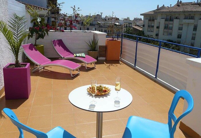 Hotel Alexandra's gay-friendly rooftop terrace. Lounge chairs, table with champagne, blue chairs, and city views. A perfect spot for gay travelers.
