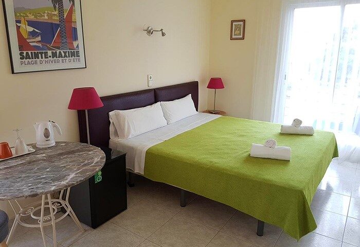 Hotel Alexandra gay-friendly room. Double bed with green cover, towels, and a table with kettle. Comfortable stay for gay travelers.