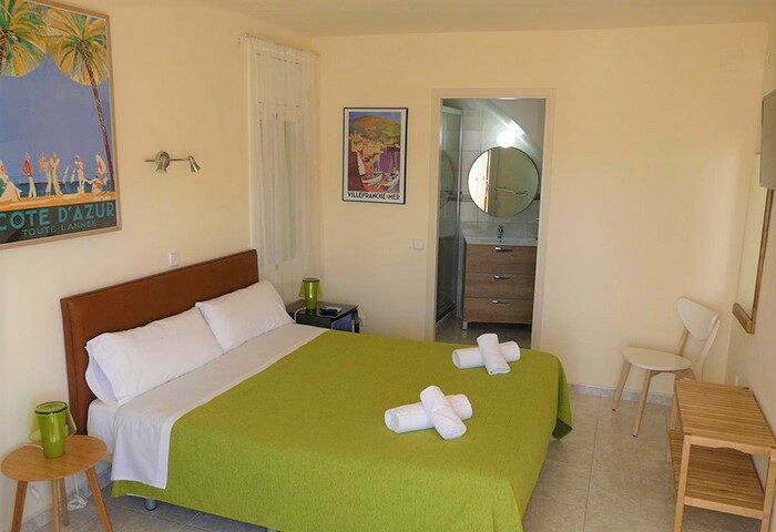 Hotel Alexandra's gay-friendly room features a double bed with a green cover, two rolled towels, and vintage travel posters. The bathroom is ensuite.