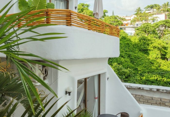 Hotel Amaca Puerto Vallarta adults-only gay-friendly hotel. Balcony view with table and chairs, lush greenery, and white building.