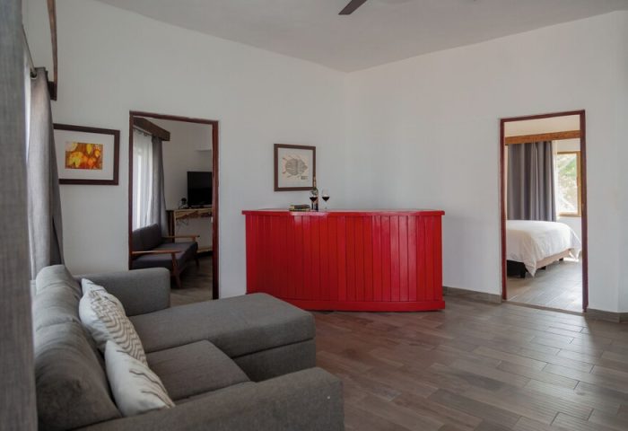 Hotel Amaca Puerto Vallarta Adults Only suite interior. Gay-friendly hotel room with red bar, gray sofa, and bedroom view. Stylish adults-only stay.