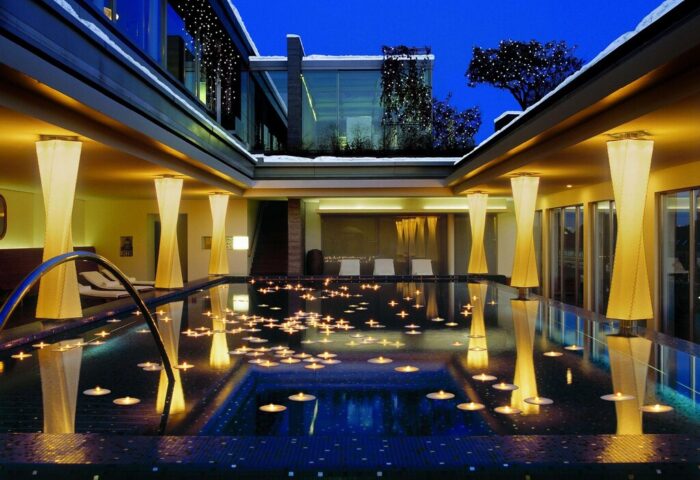 Hotel Bayerischer Hof's gay-friendly pool at night. Candles float on the water, reflecting the soft light from the modern lamps. Luxurious.