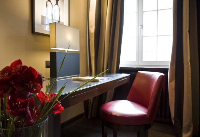 Hotel Bayerischer Hof's gay-friendly room: desk with lamp, red chair, flowers, and window. A comfortable space for gay travelers in Munich.