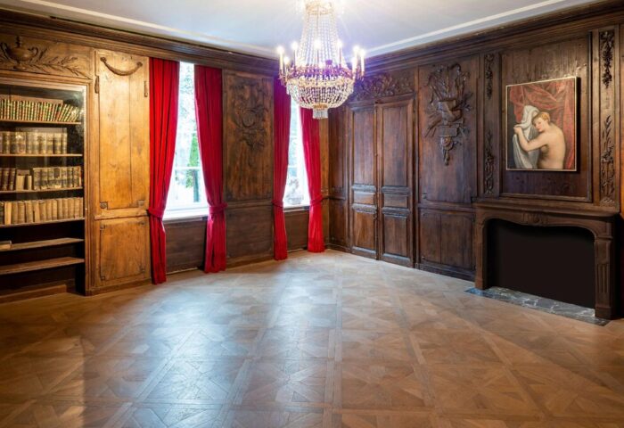 Hotel Bayerischer Hof's gay-friendly room with wood paneling, red drapes, chandelier, bookcase, painting, and fireplace. Elegant interior design.