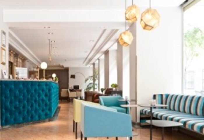 Hotel Beethoven Wien lobby. Gay-friendly hotel with modern design, turquoise reception desk, stylish seating, and geometric pendant lights.
