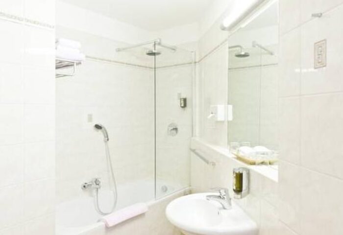 Bathroom at Gay-Friendly Hotel Beethoven Wien. White tiled walls, sink, shower, and bathtub. Modern design. Ideal for gay men travel.