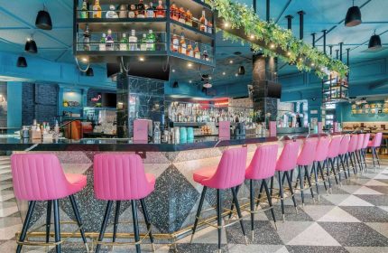 Hotel Belmont Vancouver Mgallery's bar area. Gay-friendly hotel with pink bar stools, a fully stocked bar, and a stylish black and white floor.