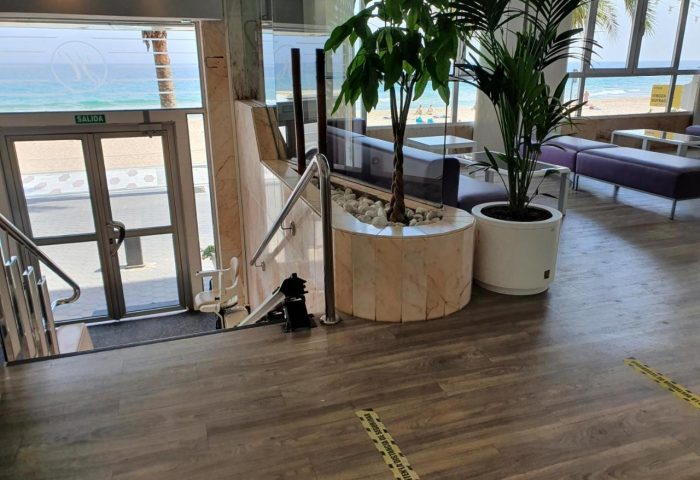 Hotel Bilbaino, a gay-friendly hotel. Lobby interior with beach view, plants, and seating. Accessibility lift for inclusive travel.