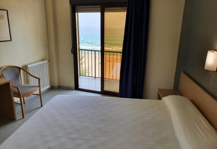 Hotel Bilbaino room with sea view. Gay-friendly hotel featuring a bed, chair, and balcony overlooking the beach. Perfect for gay travel.