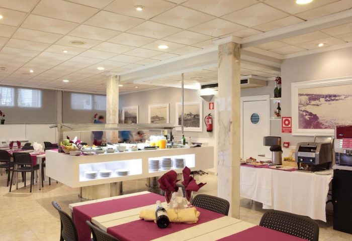 Hotel Bilbaino's dining area, a gay-friendly hotel. Breakfast buffet with plates, juice, and fruit. Tables with purple linens, wine, and glasses.