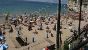 Hotel Bilbaino, a gay-friendly hotel: Crowded beach scene with sunbathers, umbrellas, and palm trees. Ideal for gay travel.