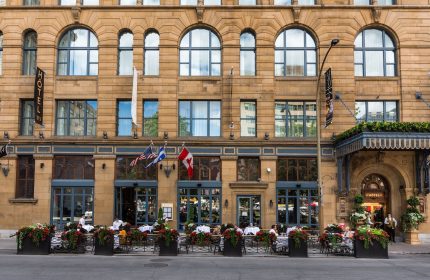 Hotel Birks Montreal facade. Gay-friendly hotel with outdoor dining, flags, and elegant architecture. A top choice for gay travel in Montreal.