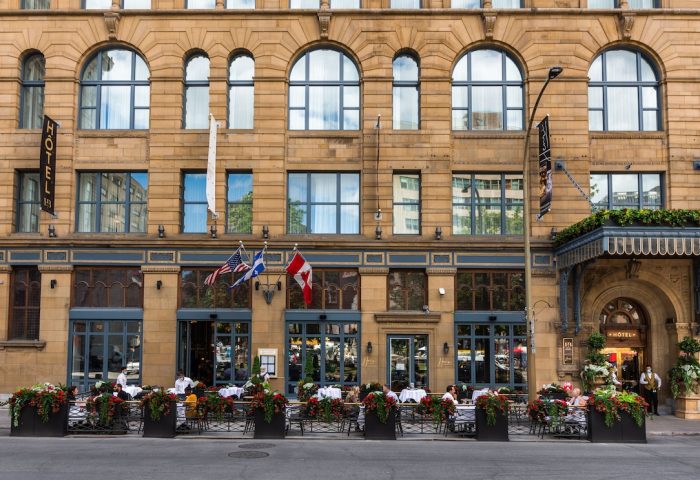Hotel Birks Montreal facade. Gay-friendly hotel with outdoor dining, flags, and elegant architecture. A top choice for gay travel in Montreal.