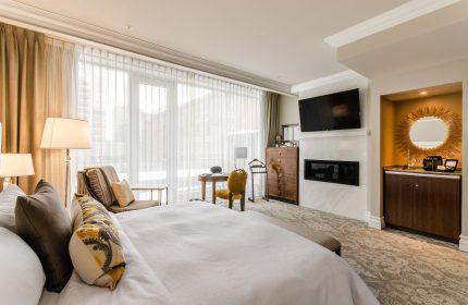 Hotel Birks Montreal's gay-friendly room. Luxurious bedroom with a large bed, fireplace, TV, desk, and city view. Upscale travel for gay men.