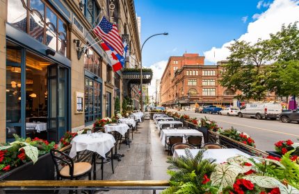 Hotel Birks Montreal's gay-friendly outdoor dining. Flags, tables with white cloths, and flowers line the street. Perfect for gay travel.