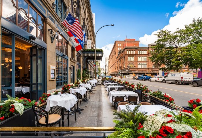 Hotel Birks Montreal's gay-friendly outdoor dining. Flags, tables with white cloths, and flowers line the street. Perfect for gay travel.