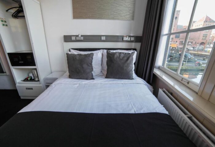 Hotel CC gay-friendly hotel room interior. Double bed with gray pillows, safe, and canal view. Modern design for gay men travelers.