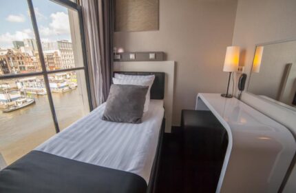 Hotel CC gay-friendly hotel room in Amsterdam. Single bed near a window with a canal view. Modern decor, desk, lamp, and comfortable bedding.