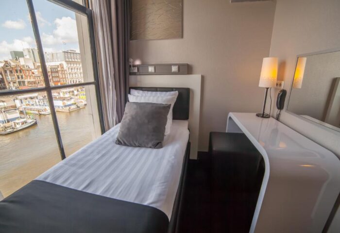 Hotel CC gay-friendly hotel room in Amsterdam. Single bed near a window with a canal view. Modern decor, desk, lamp, and comfortable bedding.