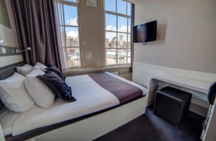 Hotel CC Gay-Friendly Hotel room. Bed with pillows, desk, stool, and TV. Canal view from window. Amsterdam gay travel lodging.
